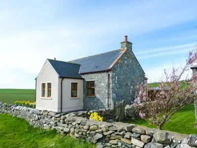 a small stone house with a stone wall at South Milton Cottage in Glenluce