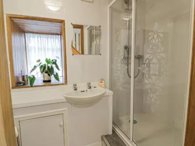 a white bathroom with a sink and a shower at The Old Brewery Store in Gatehouse of Fleet