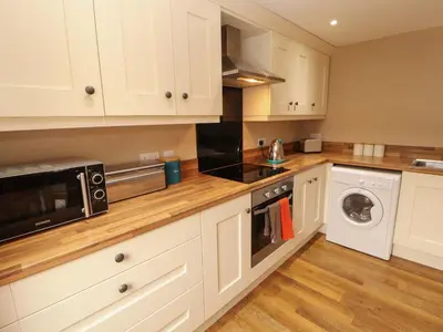 a kitchen with white cabinets and a washer and dryer at The Old Bothy in Wigton