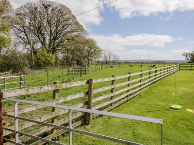 a wooden fence in a field with horses in the distance at The Old Bothy in Wigton