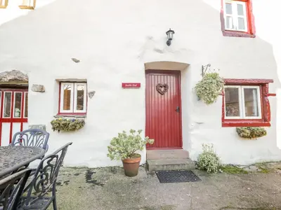 a white house with a red door and a table and chairs at Stable End Cottage in Nether Wasdale