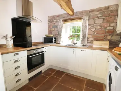 a kitchen with white cabinets and a stone wall at Faraway Cottage in Kirklinton