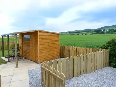 a wooden cabin with a fence in a field at Simmer Dim in Kirkbean