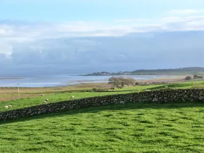 a stone wall in a field next to a body of water at Simmer Dim in Kirkbean