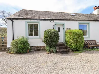 a white house with a bench and two bushes at Mell View Cottage in Watermillock