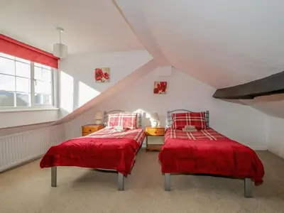 two beds in a attic bedroom with red sheets at Fountain Cottage in Keswick