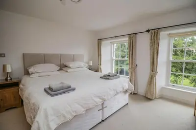 a white bedroom with a large bed with two windows at Derwentwater Apartment in Keswick