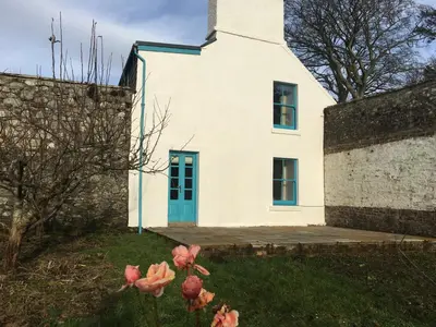 a white house with a blue door and pink flowers at Garden Cottage in Carsluith