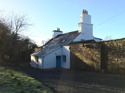 a small white house with a stone wall at Garden Cottage in Carsluith