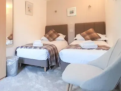 a room with two beds and a chair in it at Woodpecker Cottage in Westward