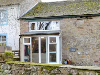 a stone house with white doors and windows at Woodpecker Cottage in Westward