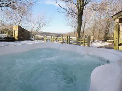a hot tub covered in snow next to a fence at Woodpecker Cottage in Westward