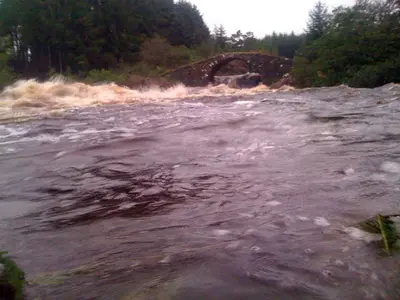 a raging river with a bridge in the background at Silver Ridge, 2 House O` Hill in Newton Stewart