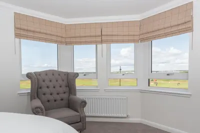 a bedroom with a chair in front of windows at Links View - Donnini Deluxe in Prestwick