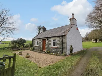 a small stone cottage with a red door in a field at Rose Cottage in Stranraer
