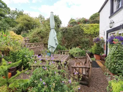 a garden with an umbrella and benches and flowers at Fell Cottage in Wigton