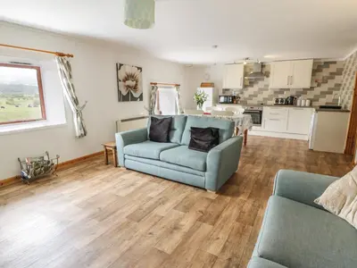 a living room with a blue couch and a kitchen at The Dairy in Newton Stewart