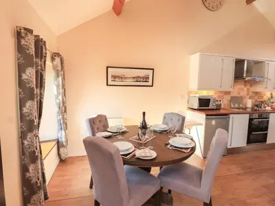 a dining room with a table and chairs and a kitchen at Stable Cottage in Wigton