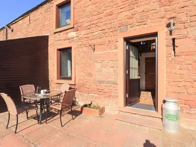 a patio with a table and chairs next to a brick building at Hayloft Cottage in Wigton