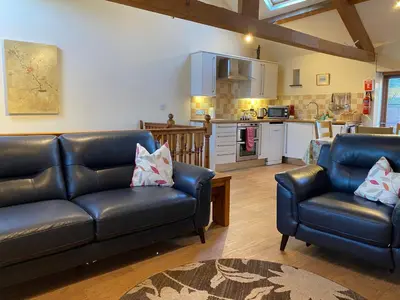 a living room with two leather couches and a kitchen at Horseshoe Cottage in Wigton