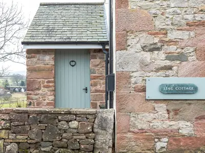 a stone building with a white door and a sign at Stag Cottage in Penrith