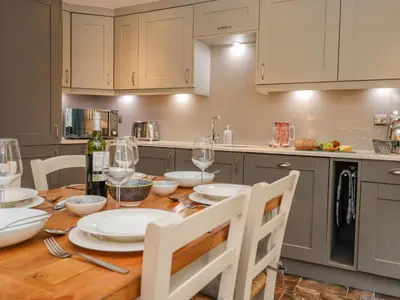 a kitchen with a wooden table with plates and wine glasses at Maple Cottage in Keswick