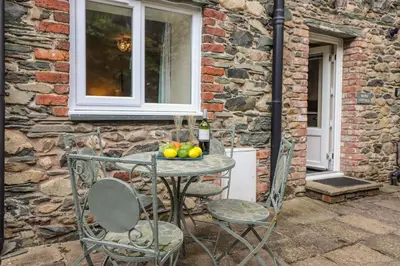 a table and chairs in front of a stone wall at Maple Cottage in Keswick