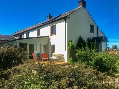 a white house with two red chairs on the porch at Low Garth Cottage in Penruddock