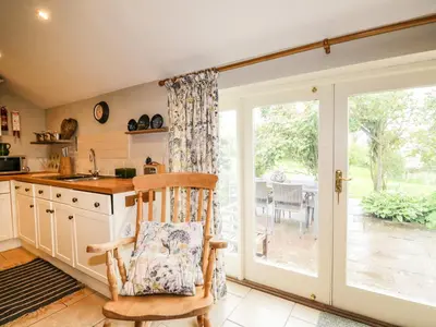 a kitchen with a rocking chair in front of a sliding glass door at Stockwell Hall Cottage in Sebergham