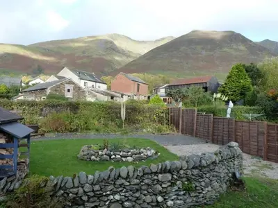 a yard with a stone wall and houses and mountains at Nightingale Cottage in Threlkeld