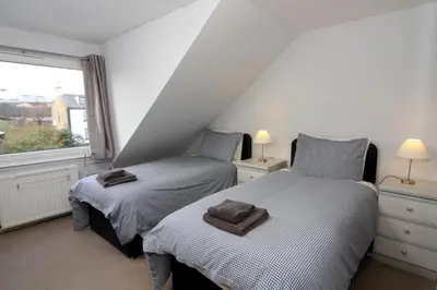 two beds in a small room with a window at Dean Park Guest House in Kilmarnock