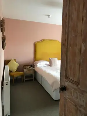 a bedroom with a bed with a yellow headboard and a chair at Netherdene Country House Bed & Breakfast in Troutbeck