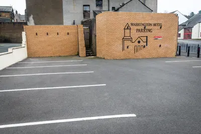 a parking lot with a brick wall with a mural at Washington Central Hotel and Sleepwell Inn in Workington