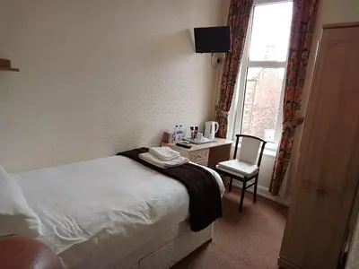 a bedroom with a bed and a chair and a window at Lindean Guest House in Dumfries