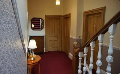 a hallway with a staircase with two doors and a lamp at Lindean Guest House in Dumfries