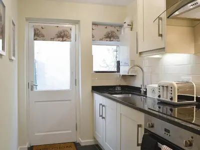 a kitchen with white cabinets and a white door at Jasmine Cottage in Keswick