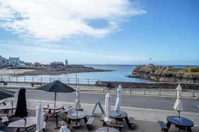 a group of tables with umbrellas and the ocean at The Waterfront in Portpatrick