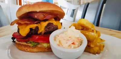 a hamburger and potato chips on a white plate with a bowl of sauce at The Waterfront in Portpatrick