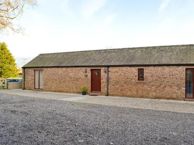 a brick building with a brown door and a driveway at The Old Byre in Dearham