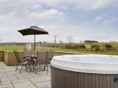 a bath tub sitting on a patio with chairs and an umbrella at The Old Byre in Dearham