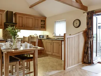 a kitchen with a table and a clock on the wall at The Old Byre in Dearham