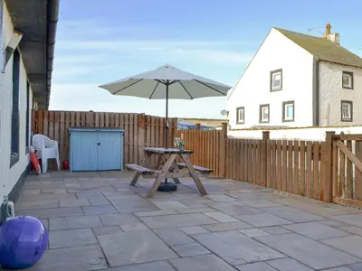 a patio with a table and an umbrella at Porthole Cottage in Allonby