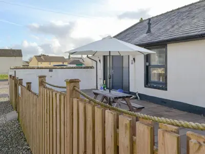a patio with an umbrella and a wooden fence at Porthole Cottage in Allonby