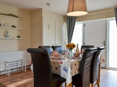 a dining room with a table with chairs and flowers on it at Porthole Cottage in Allonby