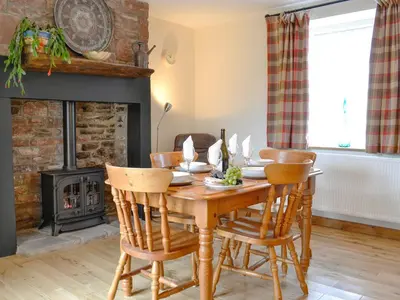 a dining room with a table and chairs and a fireplace at Brodie Cottage in Aspatria
