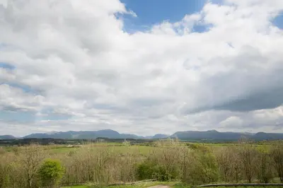 a field with a cloudy sky and mountains in the background at The Melbreak Hotel in Great Clifton