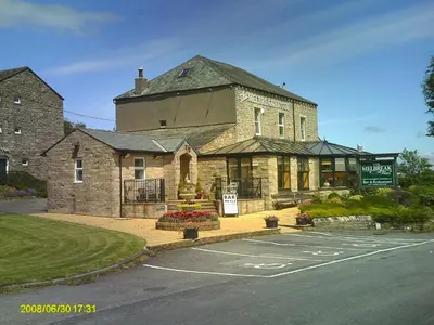 a large stone building with a sign in a parking lot at The Melbreak Hotel in Great Clifton