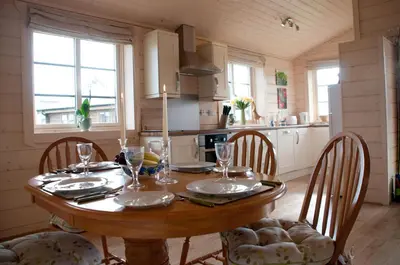 a kitchen with a wooden table with chairs and a dining room at Lapwing, Skylark & Curlew Seaside Chalets in Kirkbean