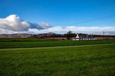 a house in the middle of a green field at Powillimount Cottage in Kirkbean