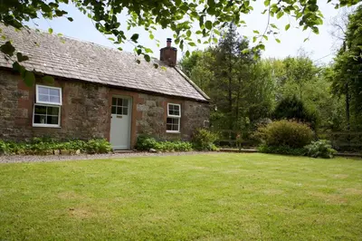 an old stone house with a grass yard at Little Dunbar Cottage in Kirkbean